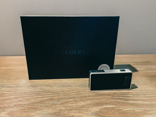 Das Blockstream Jade Plus Wallet auf einer Tischplatte liegend vor der Verpackung des Wallets